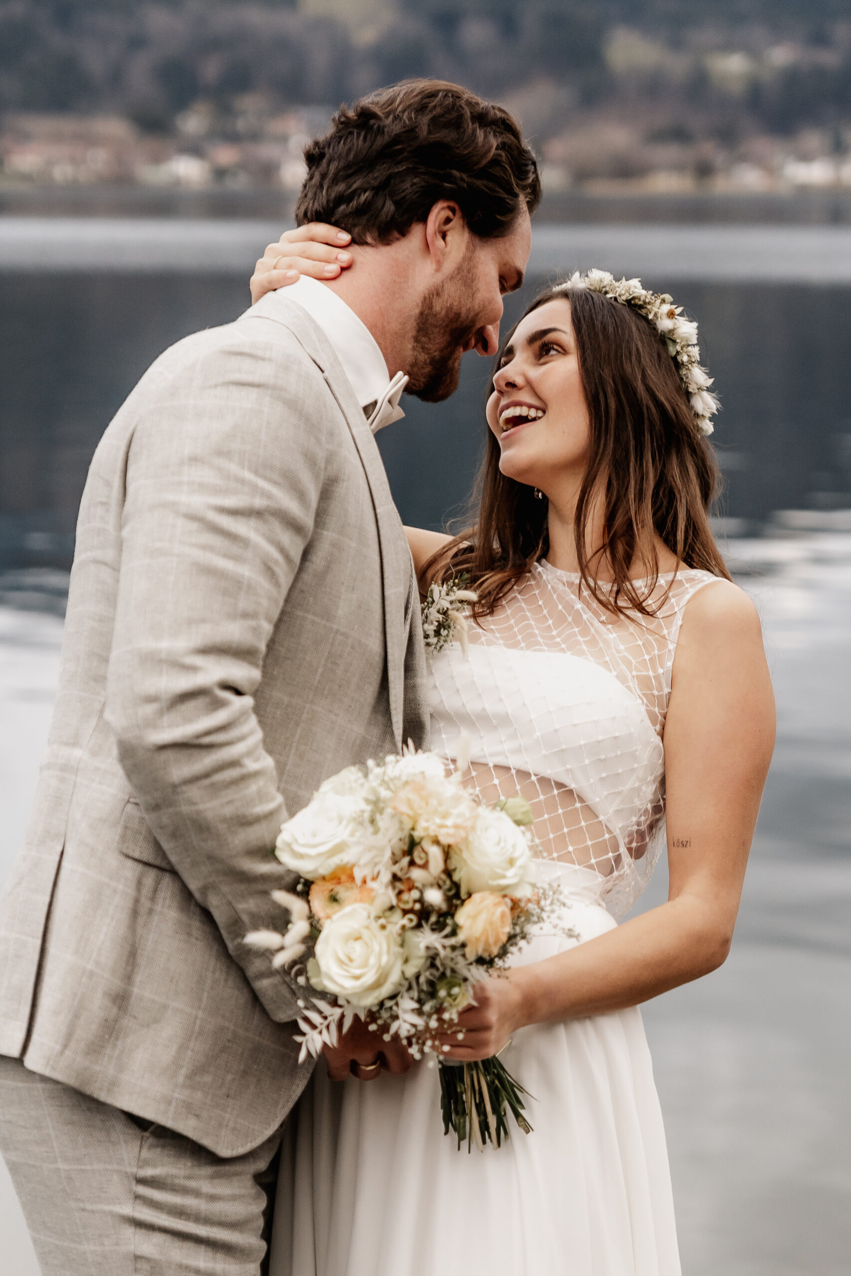 lachendes Brautpaar schaut sich verliebt vor dem Tegernsee an, Hochzeitsfotograf Tegernsee