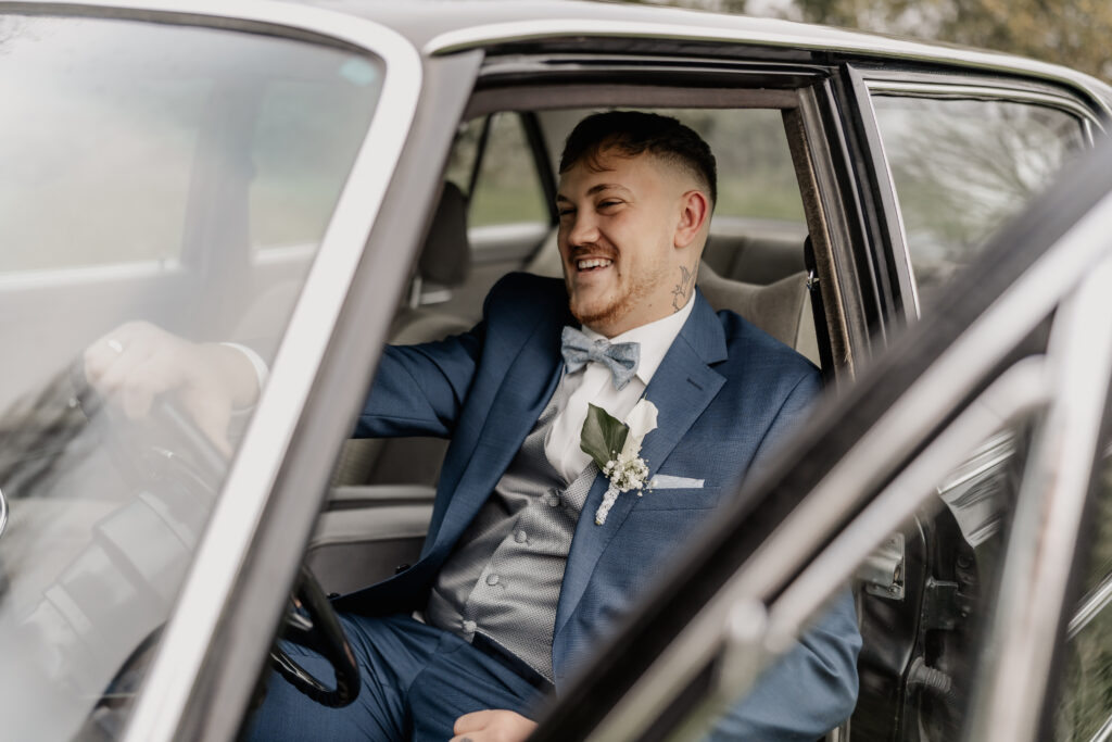 Bräutigam sitzt im Oldtimer, lächelt glücklich nach draußen, Hochzeitsfotograf Frankfurt