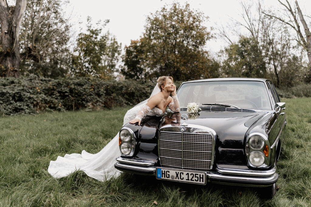 Braut auf Motorhaube eines Oldtimers, verspielt lächelnd, Vintage-Hochzeit in Eddersheim