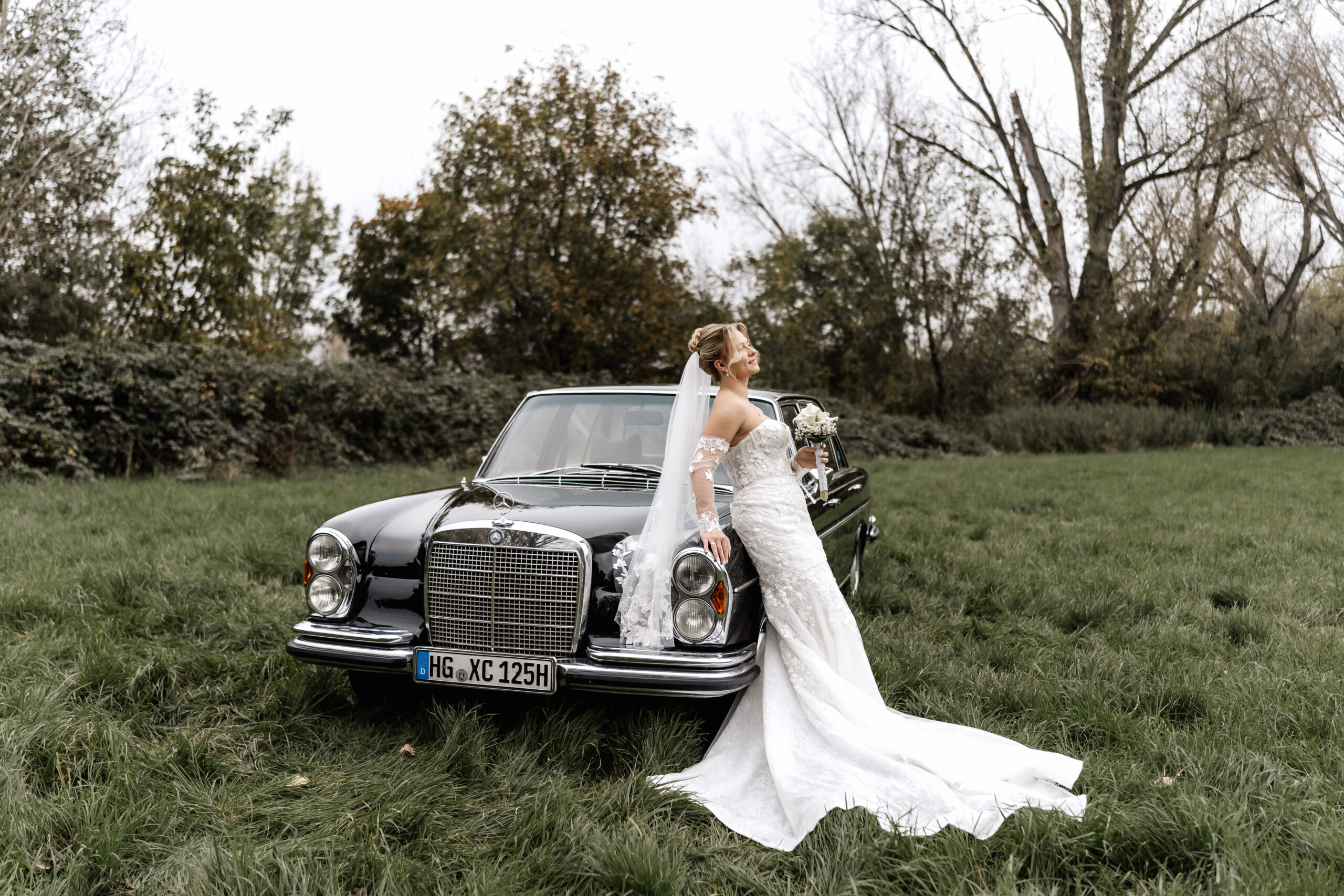 Braut lehnt sich lächelnd an einen Oldtimer. Stilvolle Hochzeitsbilder mit Oldtimer in Frankfurt
