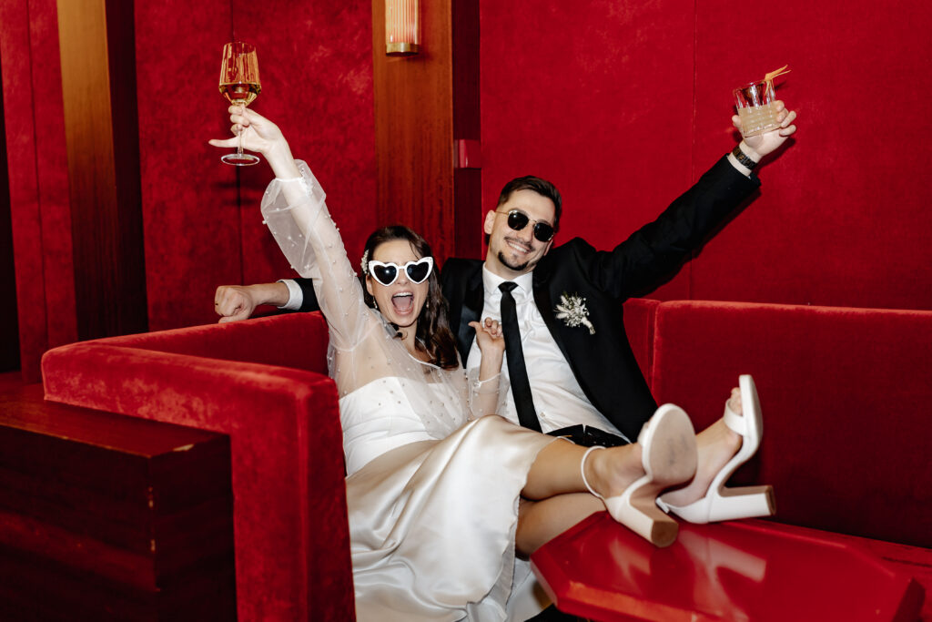 Braut und Bräutigam feiern mit Drinks in roter Lounge des Roomers Hotels – Hochzeit mit Stil