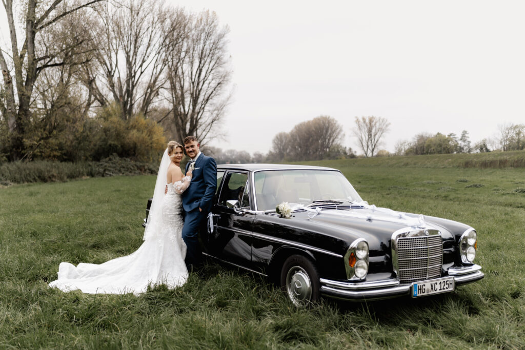 Brautpaar mit Oldtimer auf Wiese, aufgenommen von Hochzeitsfotograf Frankfurt