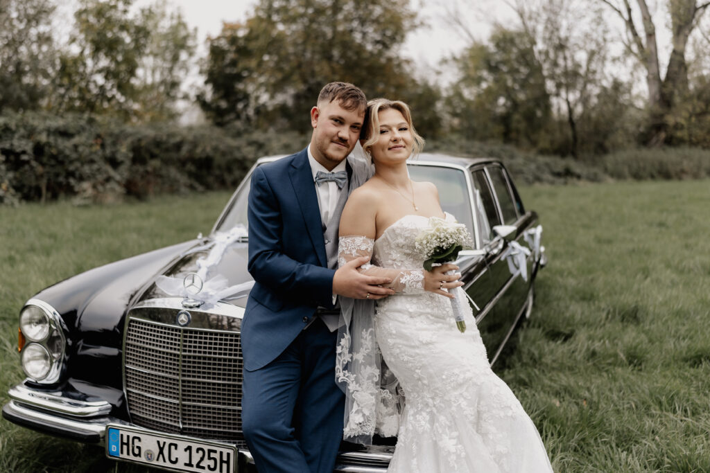 Brautpaar vor Oldtimer in Wiese – Hochzeit festgehalten von Hochzeitsfotograf Frankfurt