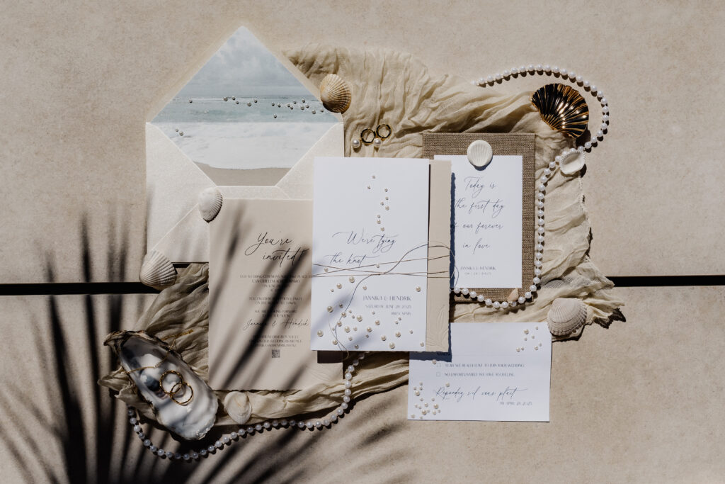 Flatlay von Hochzeitseinladungen und Eheringen mit Schatten einer Palme – künstlerisches Hochzeitsdetail auf Ibiza
