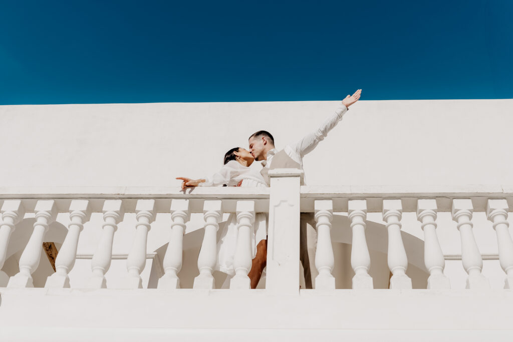 Kussmoment des Paars auf weißem Balkon mit strahlend blauem Himmel – Ibiza Wedding Photographer