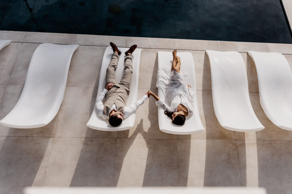 Paar hält Händchen auf weißen Liegen am Pool – Ibiza Elopement Photographer