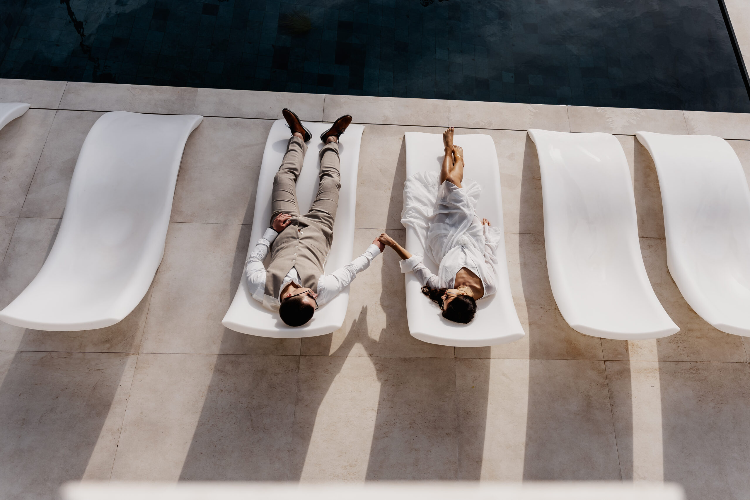 Paar hält Händchen auf weißen Liegen am Pool – Ibiza Elopement Photographer