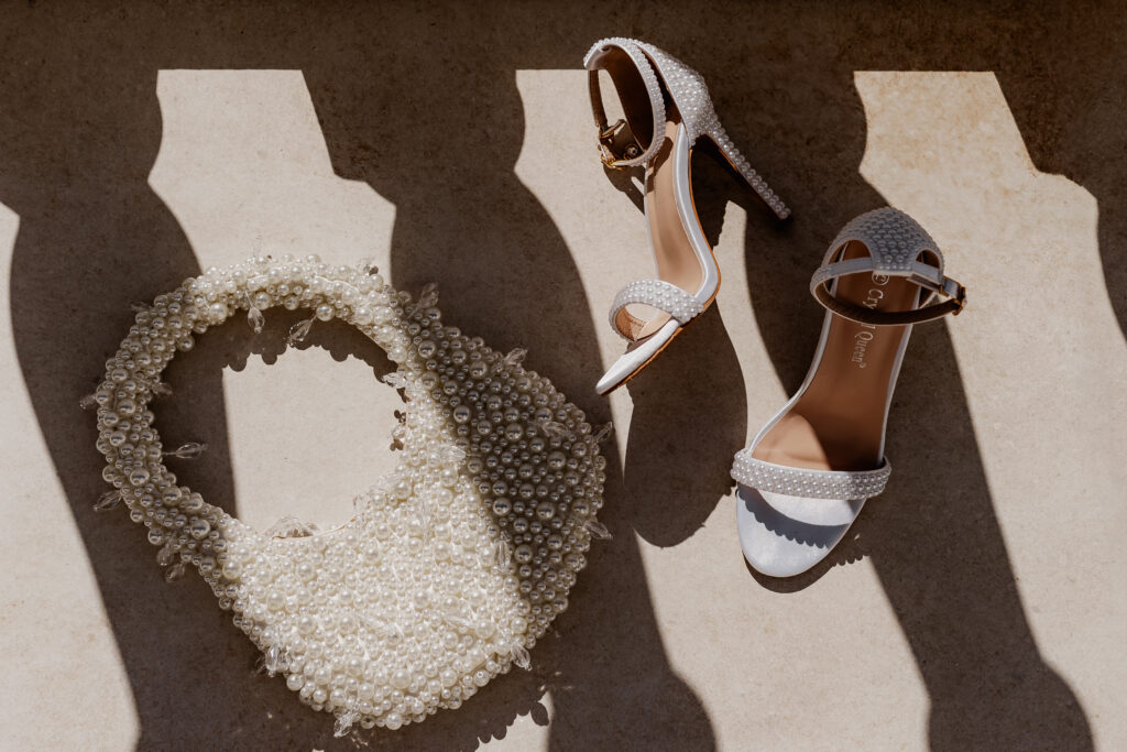 Perlentasche und weiße Brautschuhe kunstvoll im Licht-Schatten-Spiel – stilvolle Hochzeitsaccessoires einer Ibiza Elopement