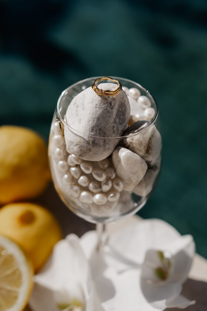 Ringe auf Stein in Glas mit Perlen und Zitronen – Detailaufnahme vom Destination Wedding Photographer