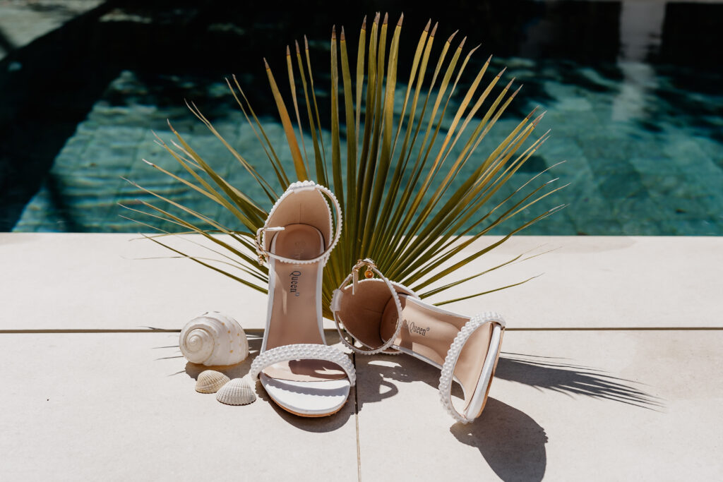 Weiße Brautsandalen mit Perlendetails, dekoriert mit Muscheln und Palmenblatt – Styling für eine Ibiza Elopement Hochzeit