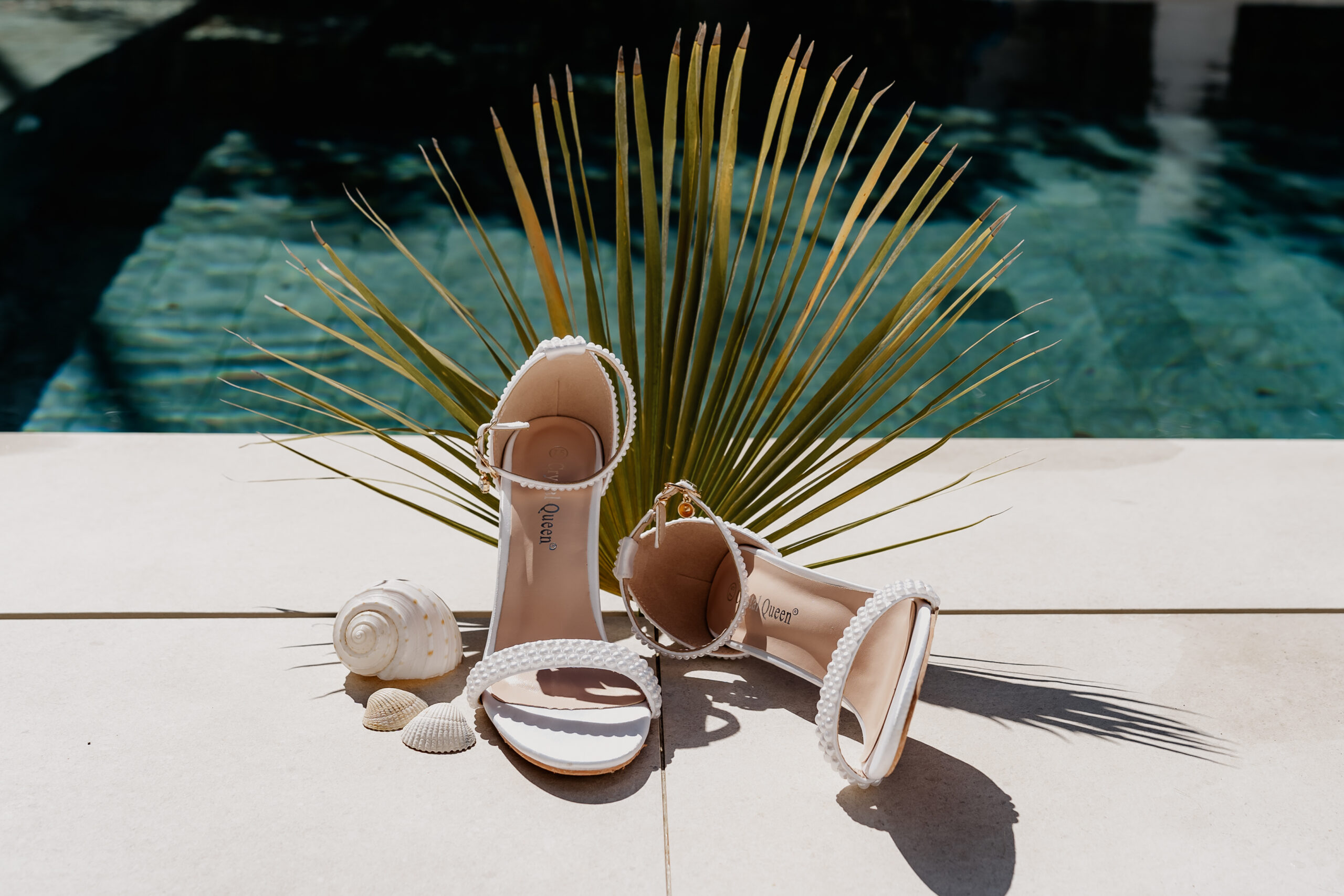 Weiße Brautsandalen mit Perlendetails, dekoriert mit Muscheln und Palmenblatt – Styling für eine Ibiza Elopement Hochzeit