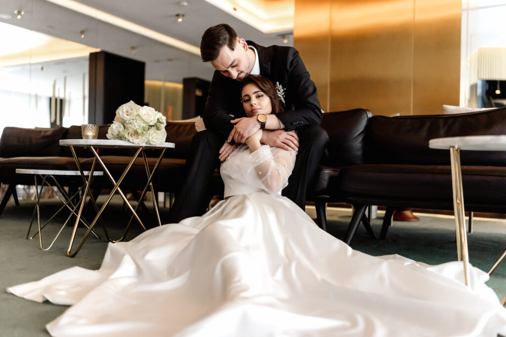 Zärtliche Umarmung des Brautpaares auf der Couch im Roomers Hotel München - Hochzeitsfotograf München.