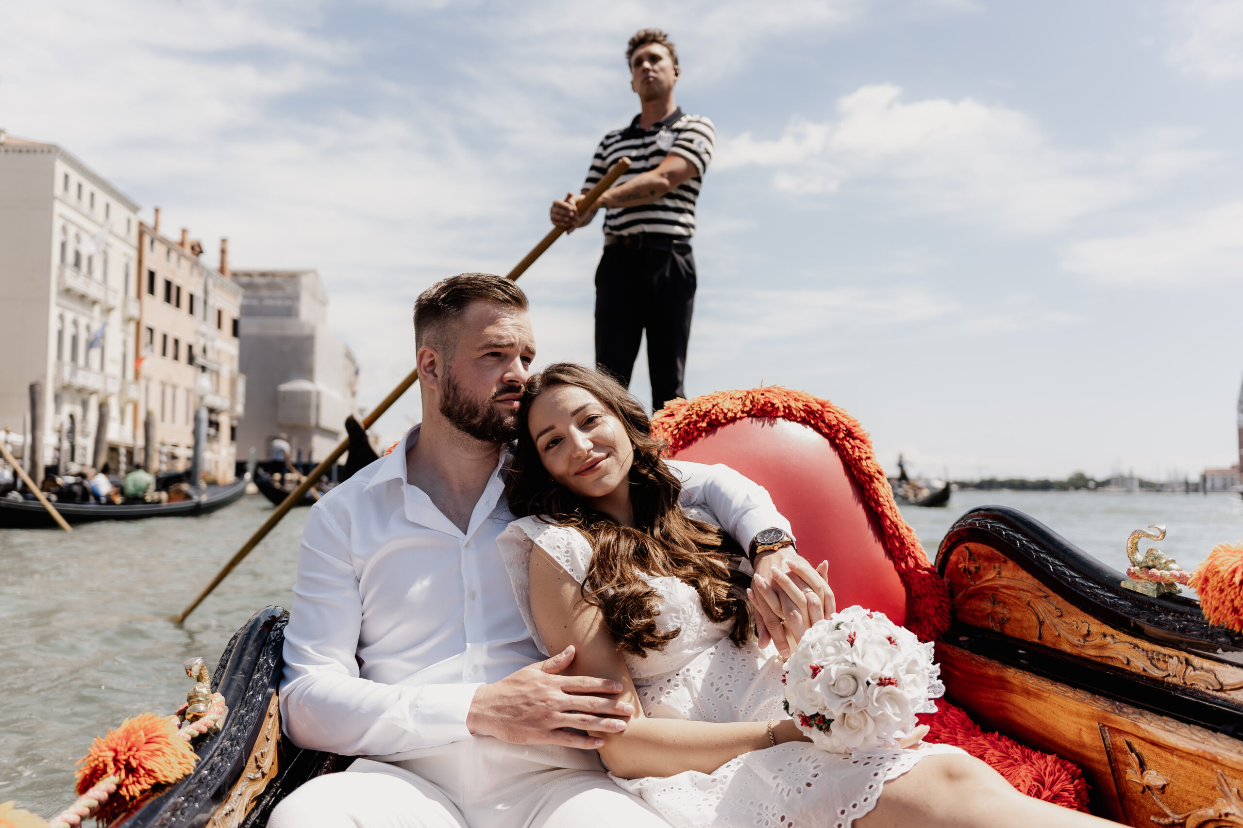 Brautpaar sitzt zufrieden in einer Gondel in Venedig, Gondoliere fährt sie, Hochzeitsfotograf Venedig