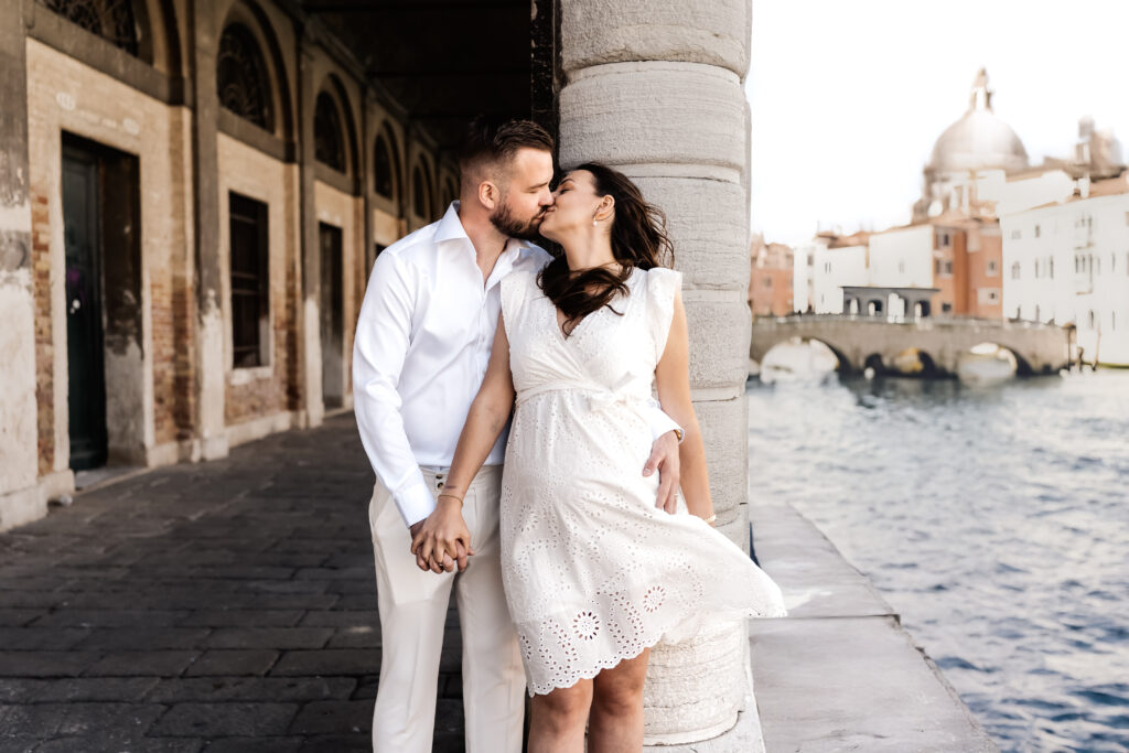 Braut und Bräutigam stehen innig am Kanal in Venedig, Kleid weht,