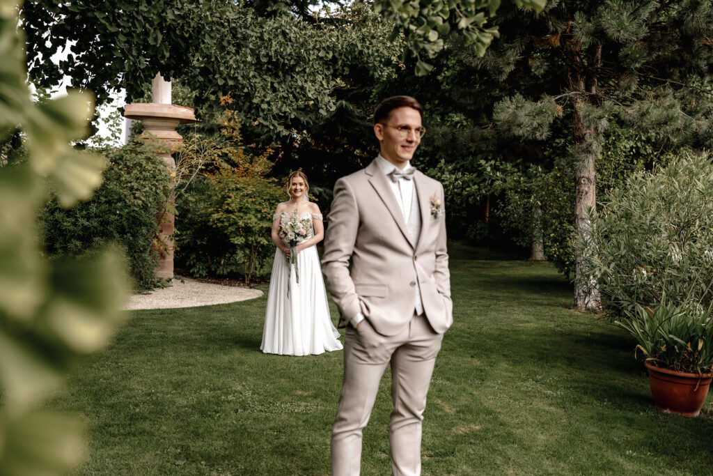 First Look im Grünen: Braut wartet lächelnd auf den Bräutigam, Hochzeit im BourdierKoeller Stetten