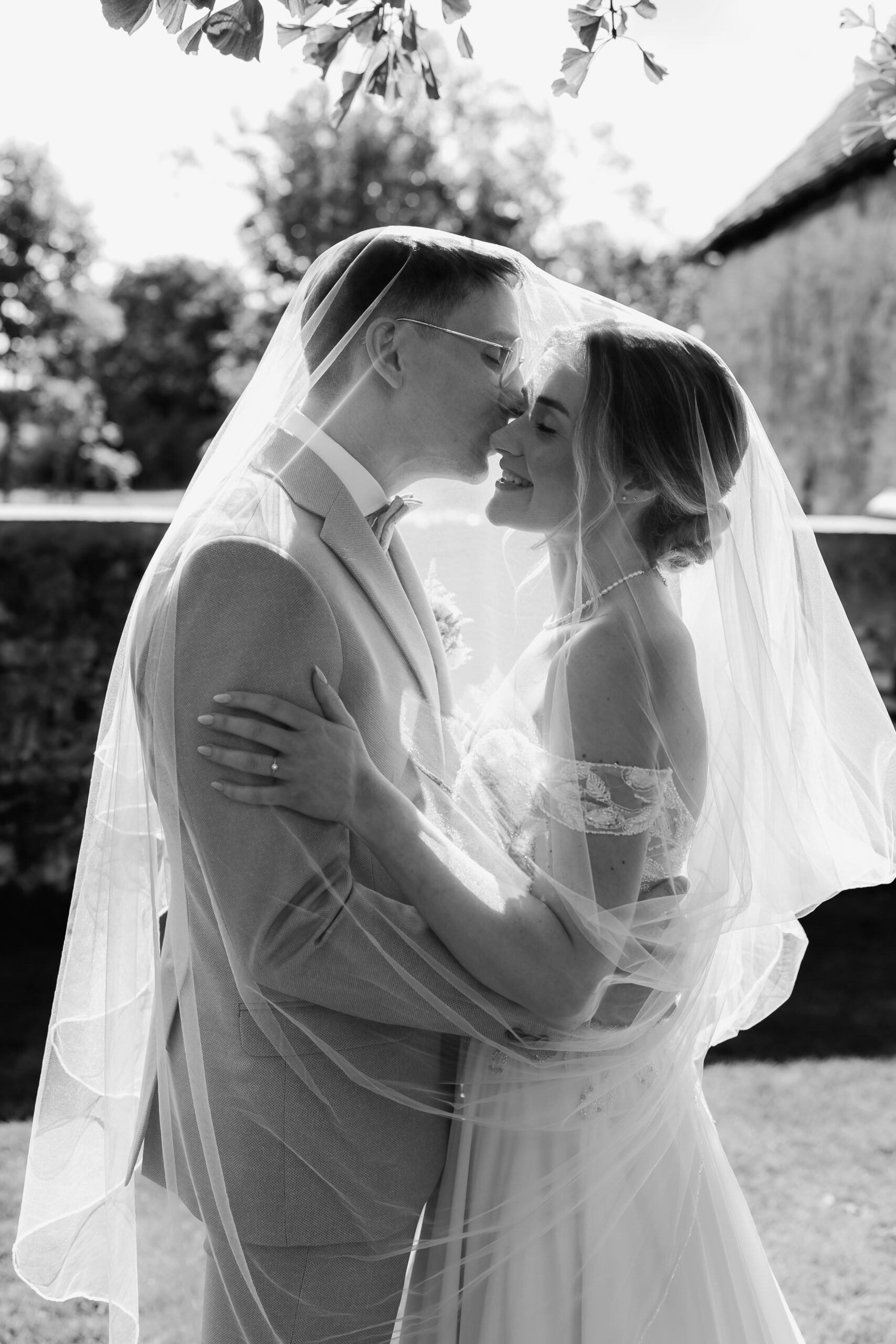 Schwarzweißfoto: Brautpaar küsst sich unter dem Schleier, emotionales Hochzeitsshooting BourdierKoeller