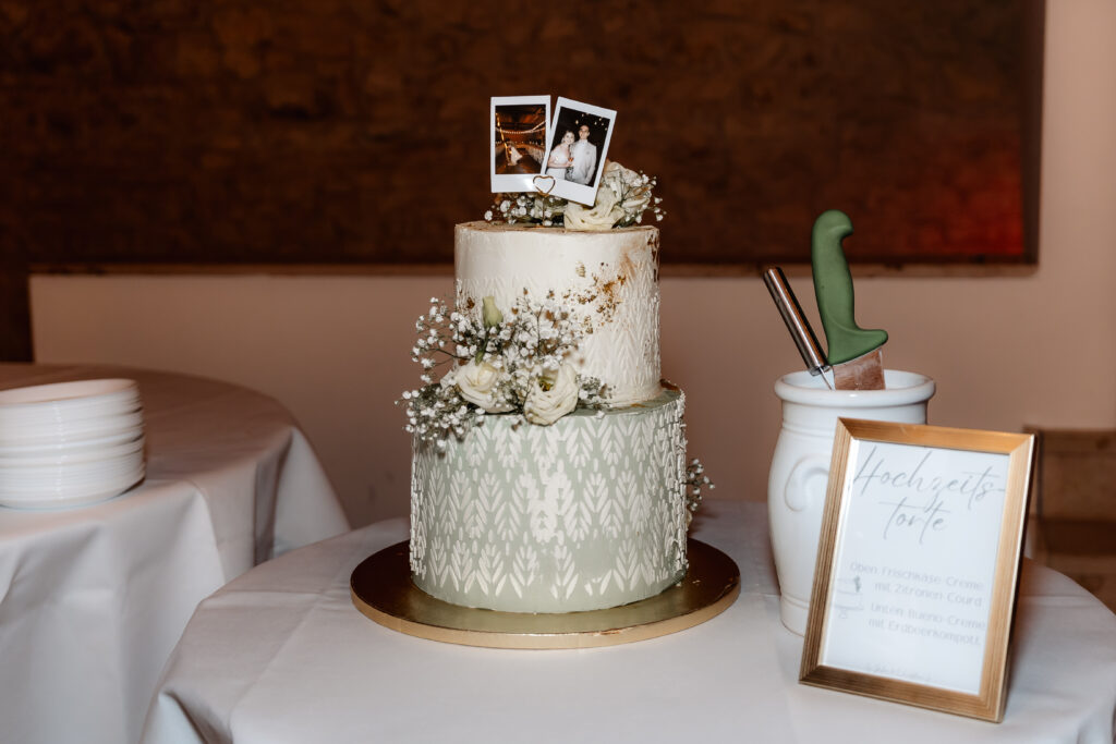 Zweistufige Hochzeitstorte mit floraler Dekoration und Polaroid-Fotos auf einem Tisch