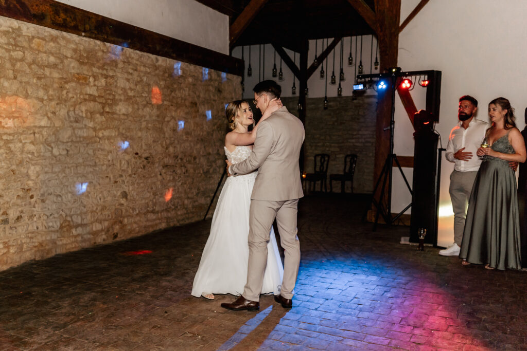 Braut und Bräutigam tanzen eng umschlungen auf der Tanzfläche im rustikalen Hochzeitssaal.
