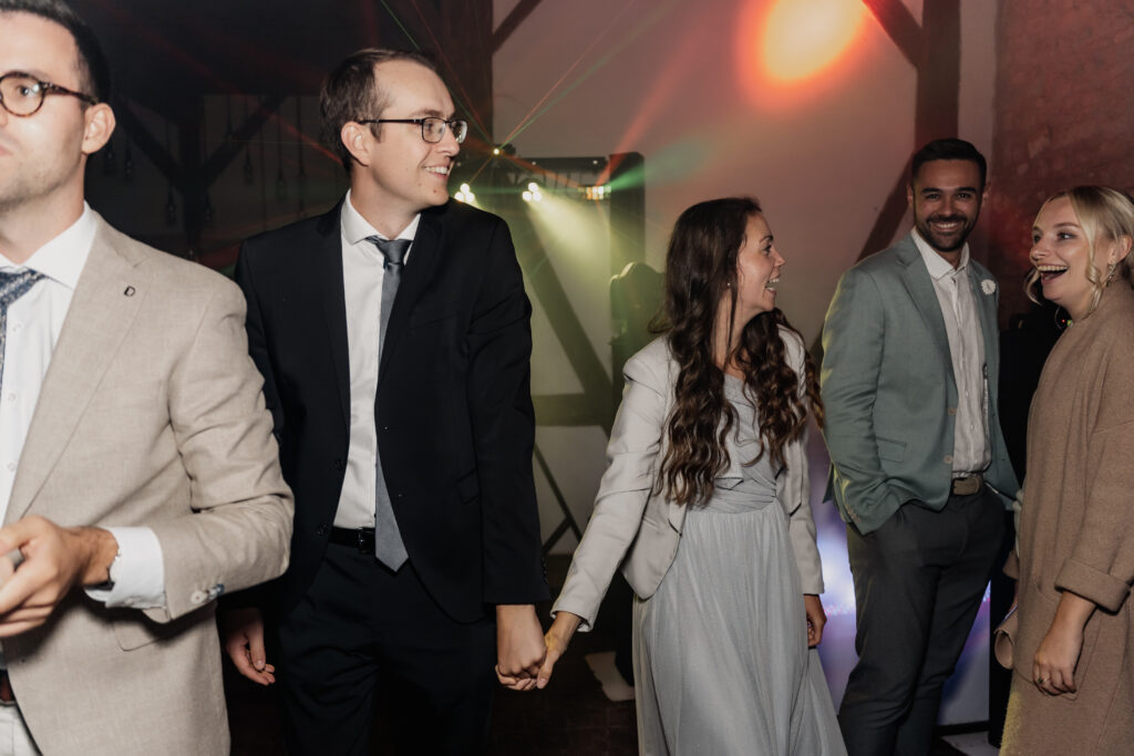 Hochzeitsgäste stehen Hand in Hand auf der Tanzfläche, fröhliche Stimmung bei der Party