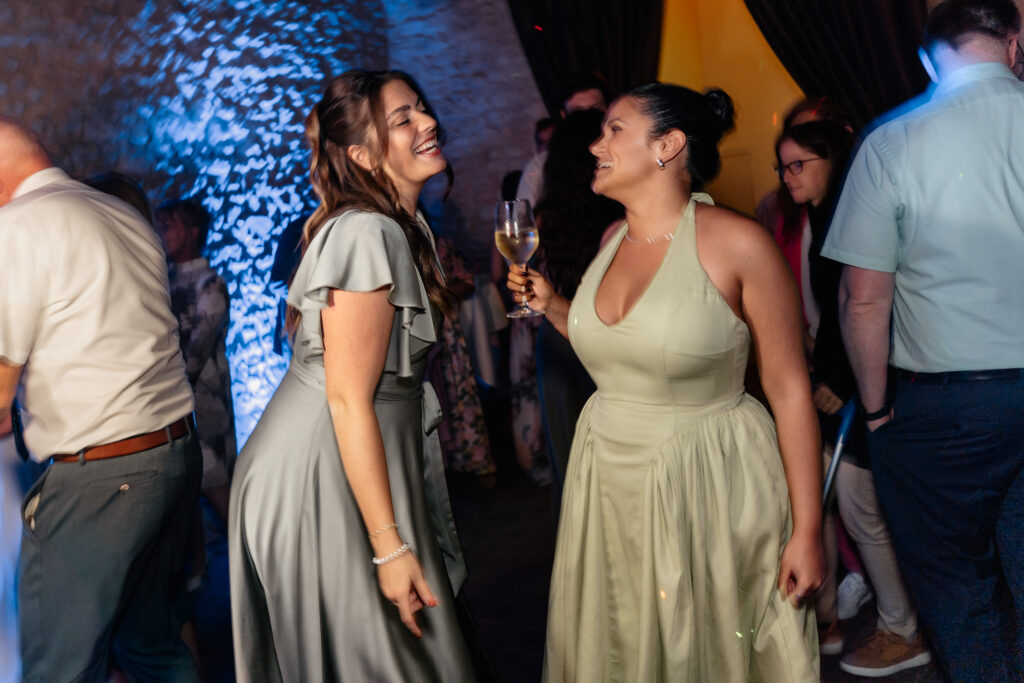 Zwei Frauen tanzen lachend mit Weinglas auf der Tanzfläche bei der Hochzeitsfeier