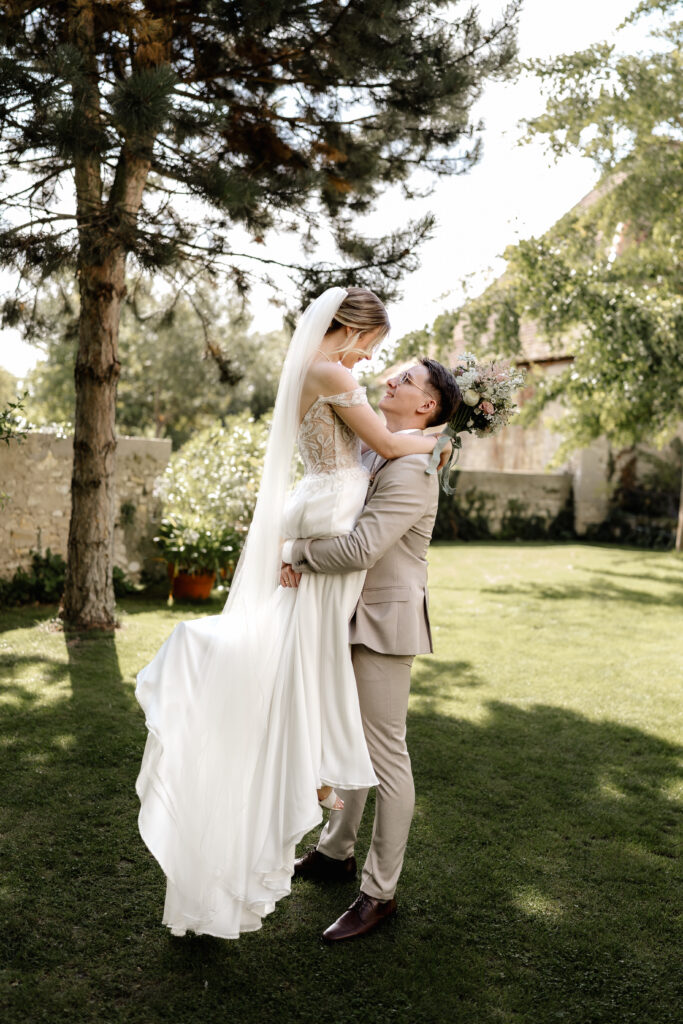 Bräutigam hebt die Braut im Garten hoch, verspieltes Brautpaarshooting BourdierKoeller Stetten