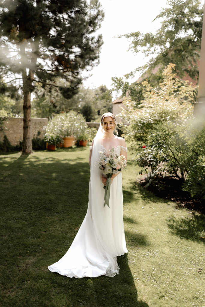 Braut steht im Garten mit Brautstrauß, elegantes Brautportrait