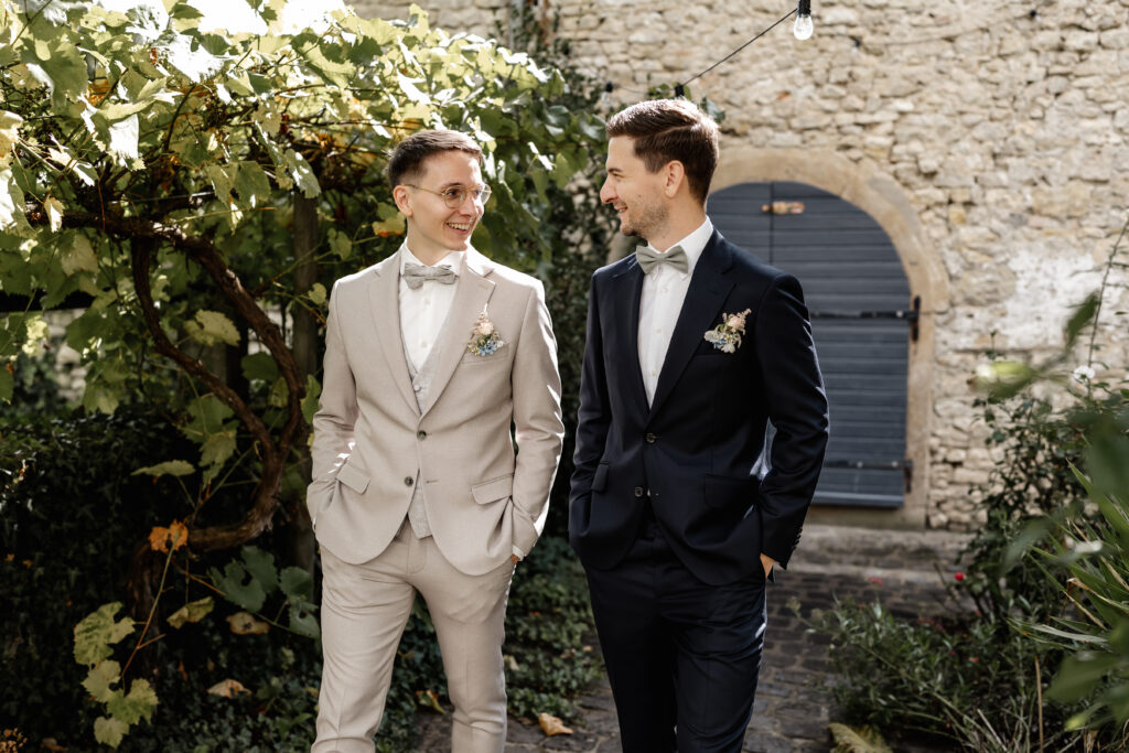 Bräutigam und Trauzeuge stehen sich lächelnd gegenüber, Hochzeitsportrait im Innenhof