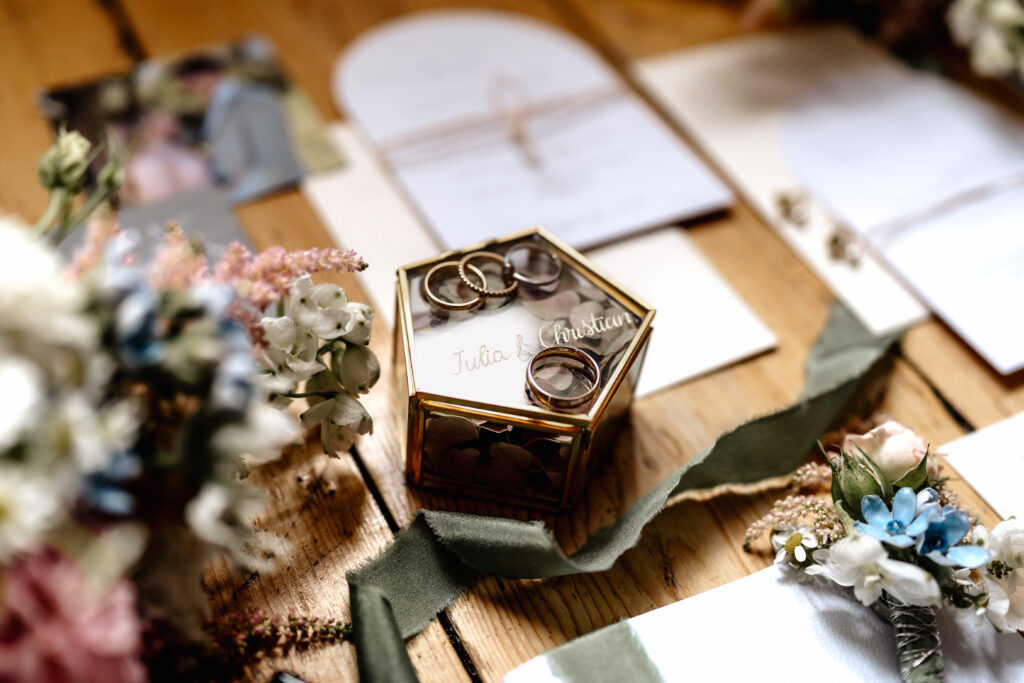 Eheringe in Glasbox mit Blumen, Detailaufnahme der Hochzeitsringe auf Holzboden