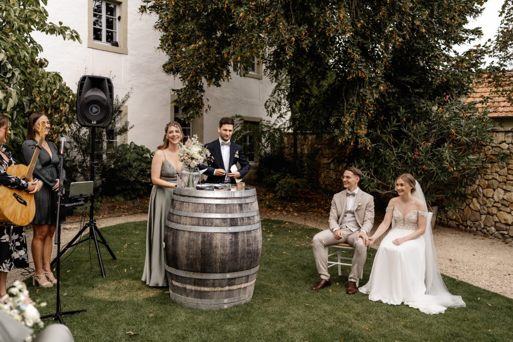 Rede bei der freien Trauung, Brautpaar sitzt lächelnd im Hintergrund