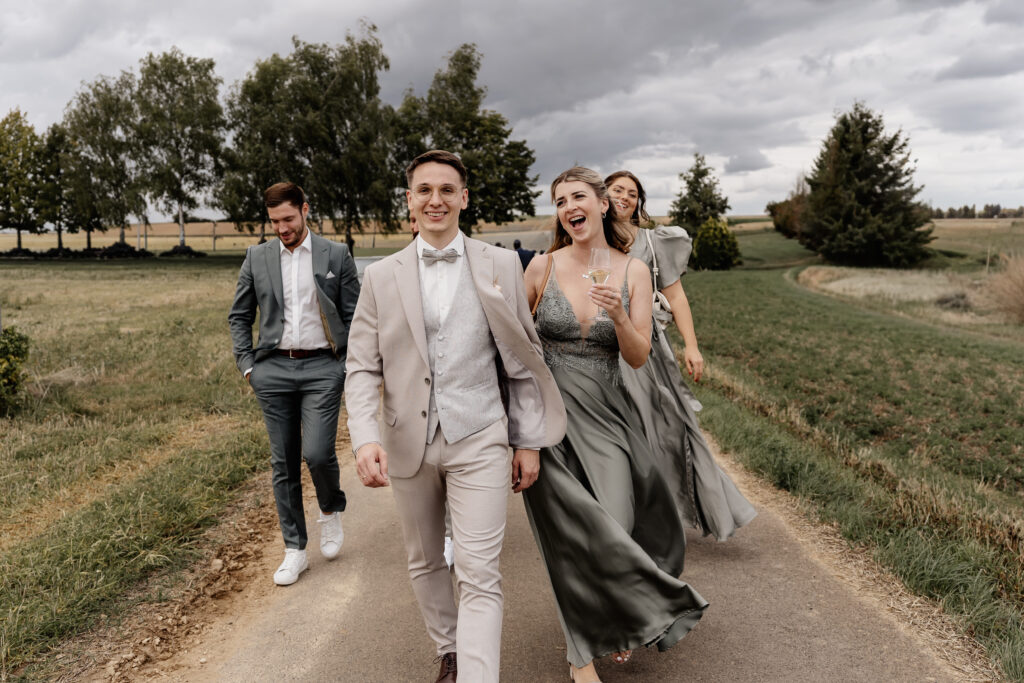 Hochzeitsgäste gehen gemeinsam mit dem Bräutigam durch die Weinberge