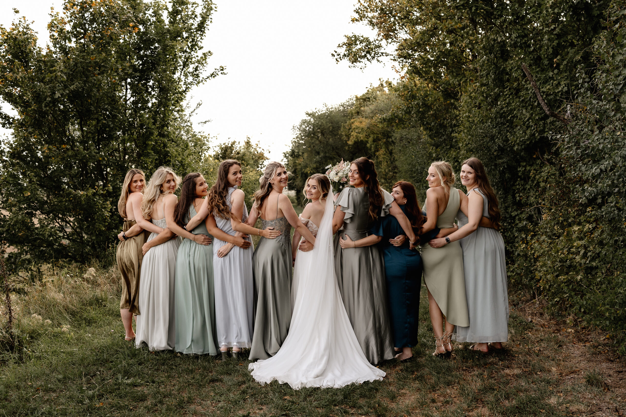 Braut und Brautjungfern stehen eng beieinander, natürliches Hochzeitsshooting im Grünen