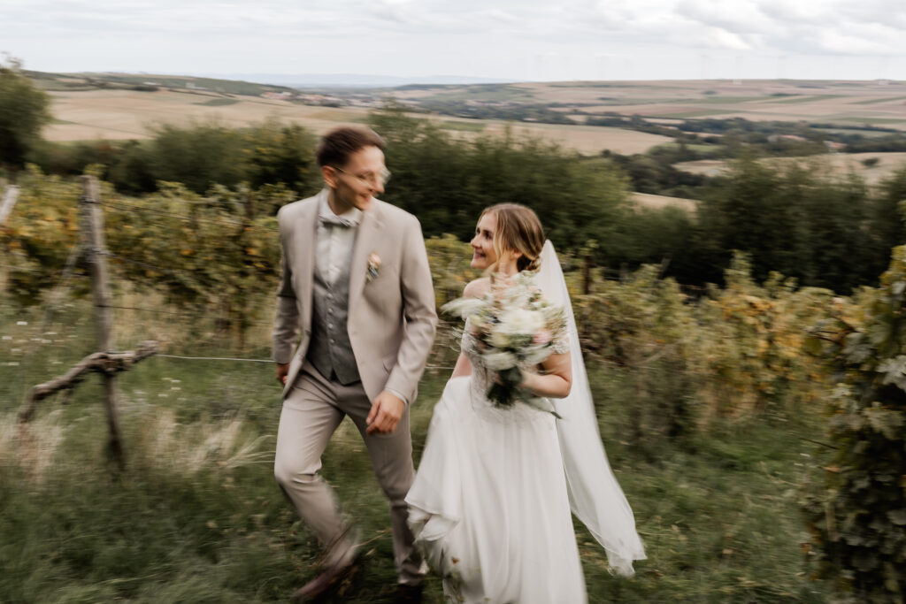 Bewegungsbild vom Brautpaar Hand in Hand in den Weinbergen
