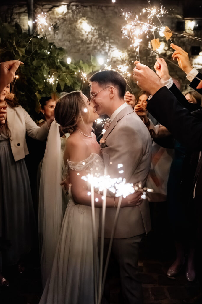 Braut und Bräutigam küssen sich umgeben von Gästen mit Wunderkerzen bei der Hochzeitsfeier