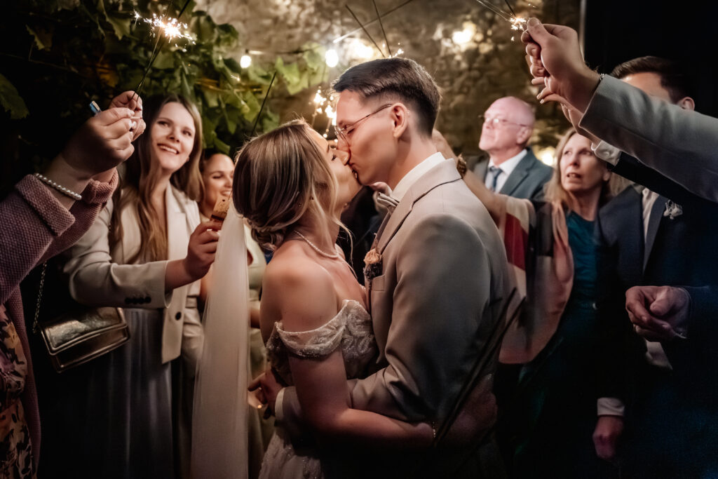 Emotionaler Kuss des Brautpaars während eines Wunderkerzen-Spaliers