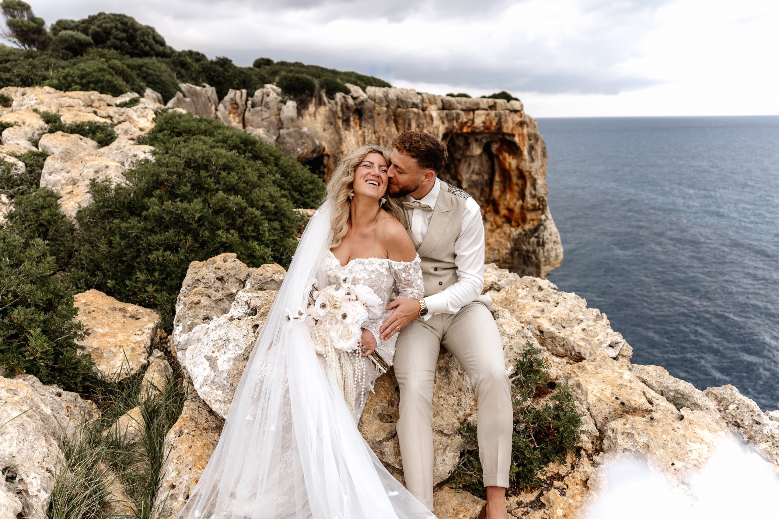 Brautpaar kuschelt bei After-Wedding-Shooting mit Blick auf Meer und Klippen Mallorca