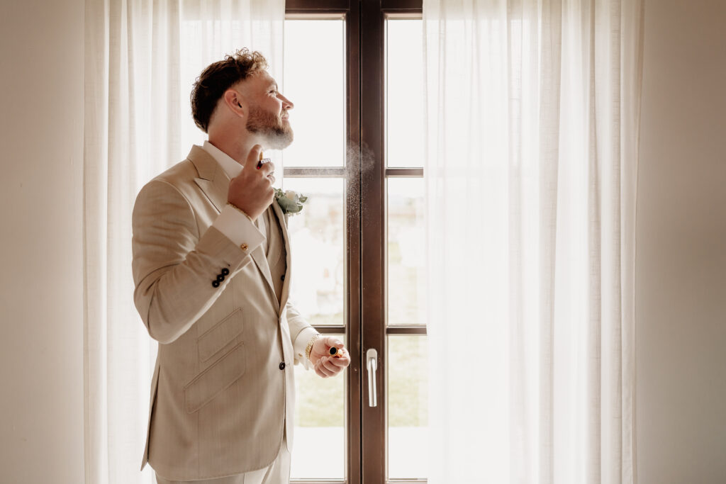 Bräutigam trägt Parfum beim Getting Ready im natürlichen Licht auf Mallorca