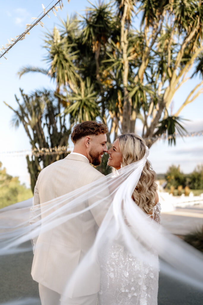 Lachendes Hochzeitspaar steht vor Palmen während Sonnenuntergang
