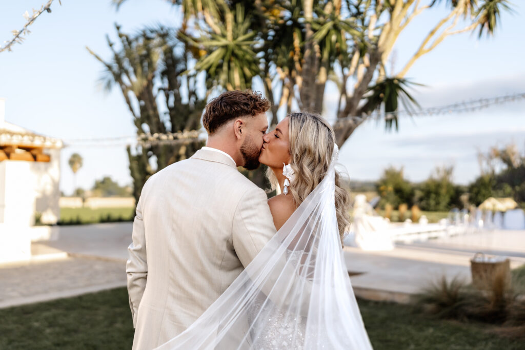 Braut und Bräutigam küsst sich liebevoll, Schleier weht im Wind auf Mallorca