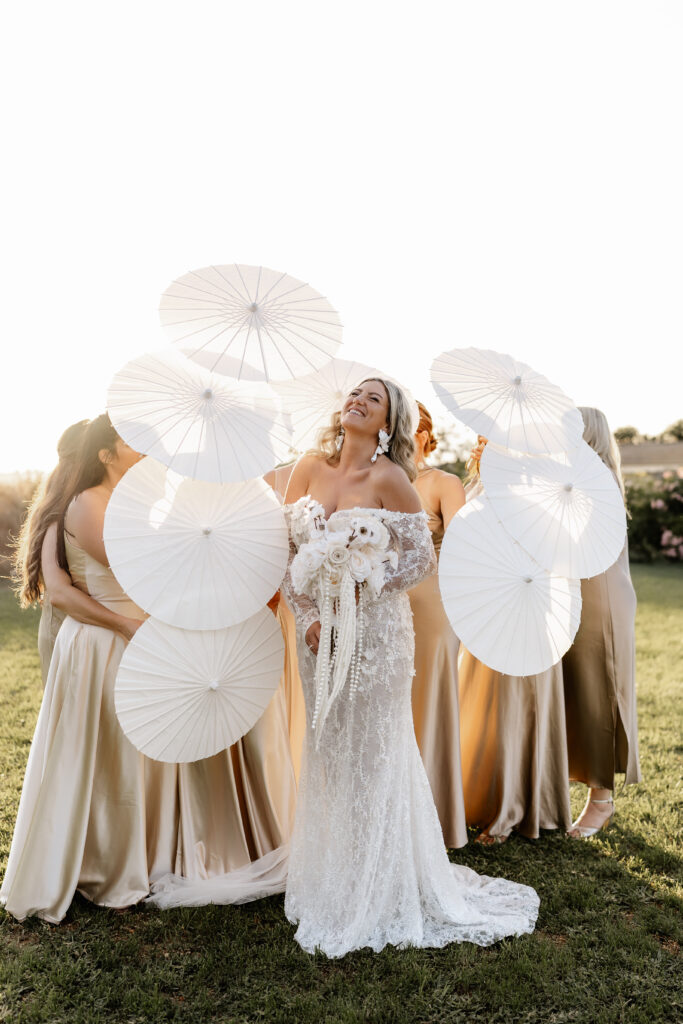 Brautjungfern stehen mit Sonnenschirmen um die Braut bei Golden Hour auf Mallorca