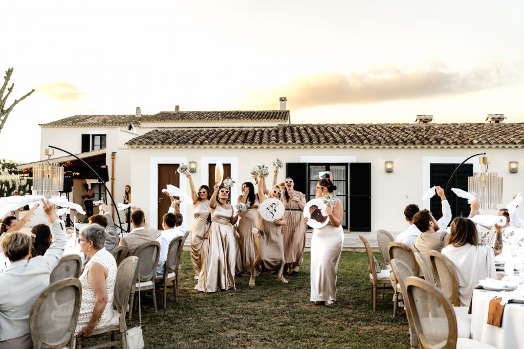 Brautjungfern tanzen mit lustigen Bildern von Braut und Bräutigam zwischen den Tischen beim Hochzeitseinlauf
