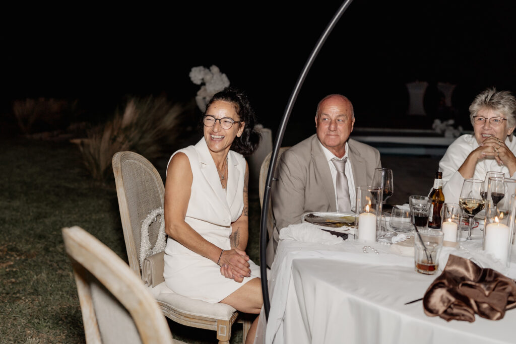 Mutter der Braut sitzt lachend am Tisch während Rede des Brautpaars