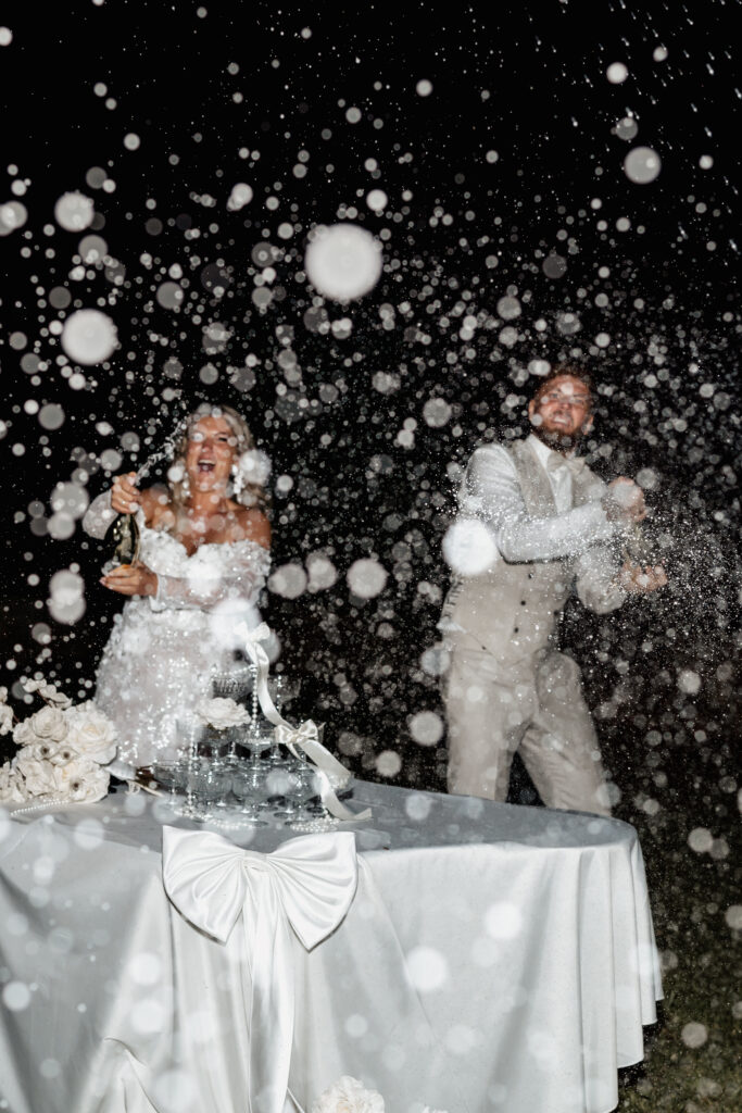 Brautpaar spritzt lachend mit Sekt bei Hochzeit am Abend