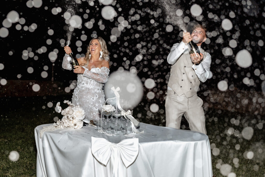 Brautpaar steht lachend am Sektturm während der Abendfeier
